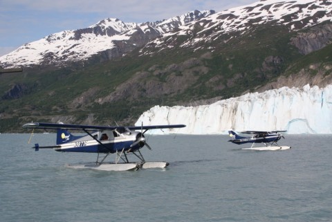 Two float planes on the water with a glacier and mountains in the background.