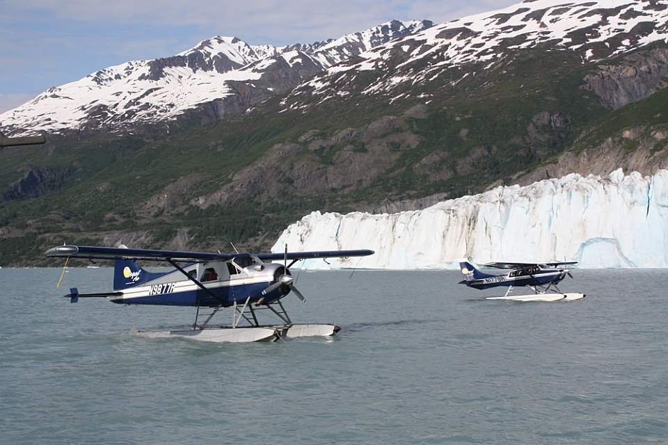Two float planes on the water with a glacier and mountains in the background.