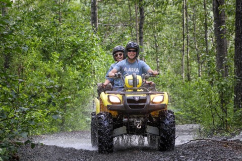 Two people ride an ATV down an Alaska forest trail.