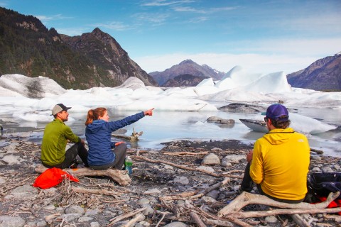 Hikers sit on a rocky beach admiring an ice-choked lagoon.