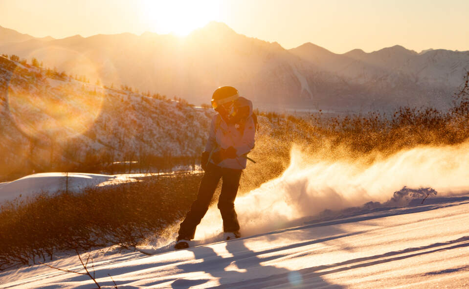 A skiier heads down the mountain at sunset