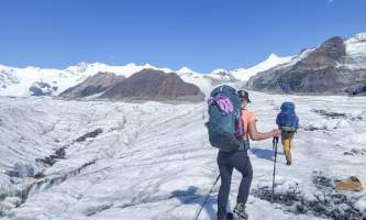 Backpackers traverse a glacier with white mountains in the background Anya Voskresensky