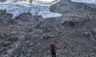 Hiker climbs a rocky rib below a hanging glacier Anya Voskresensky