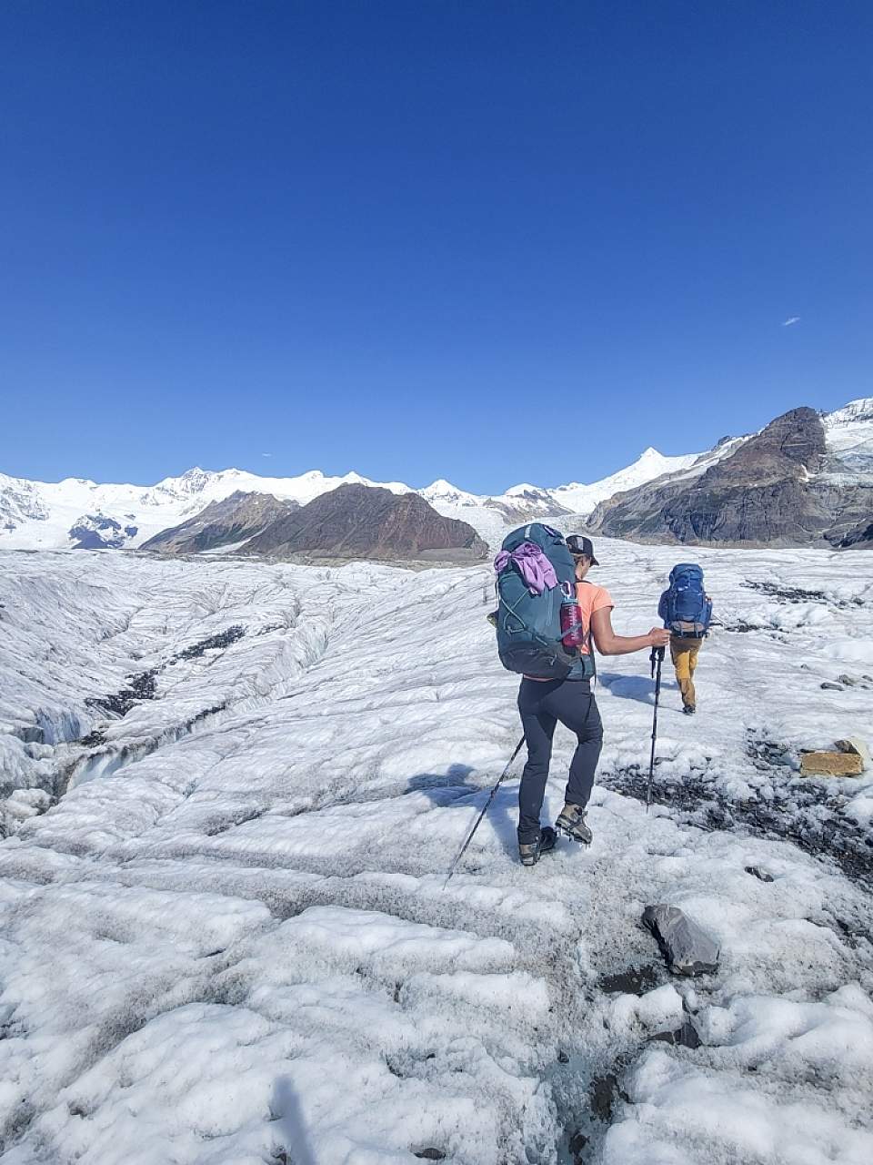 Backpackers traverse a glacier with white mountains in the background Anya Voskresensky