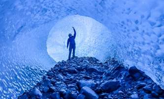 Person reaches toward the ceiling of blue ice tunnel Anya Voskresensky