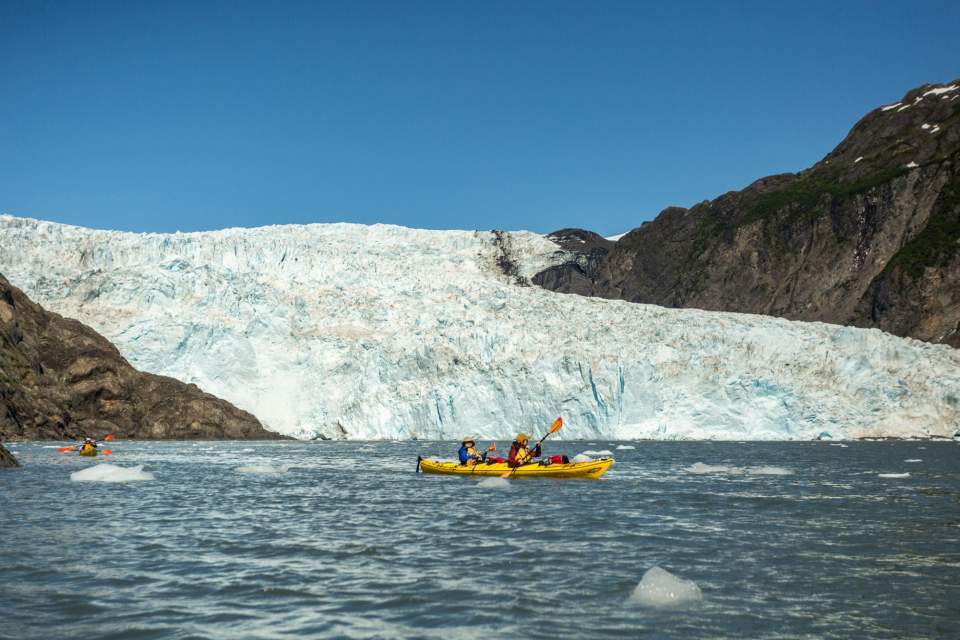 Two kayakers in front of a large, tidewater glacier