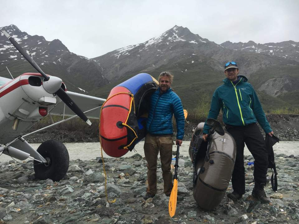 Two men carry packrafts from a floatplane to explore Alaska's national parks