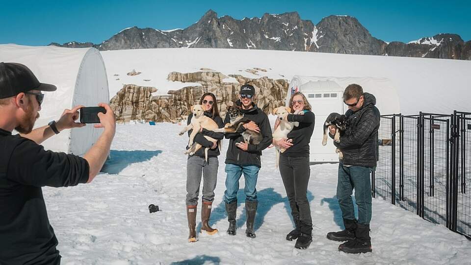 Two people hold onto husky puppies