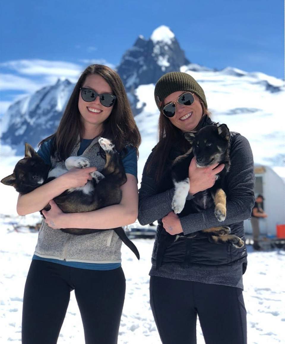 Two people hold onto husky puppies