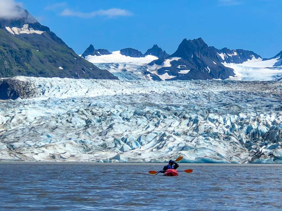 A double person kayak floats close to a glacier.