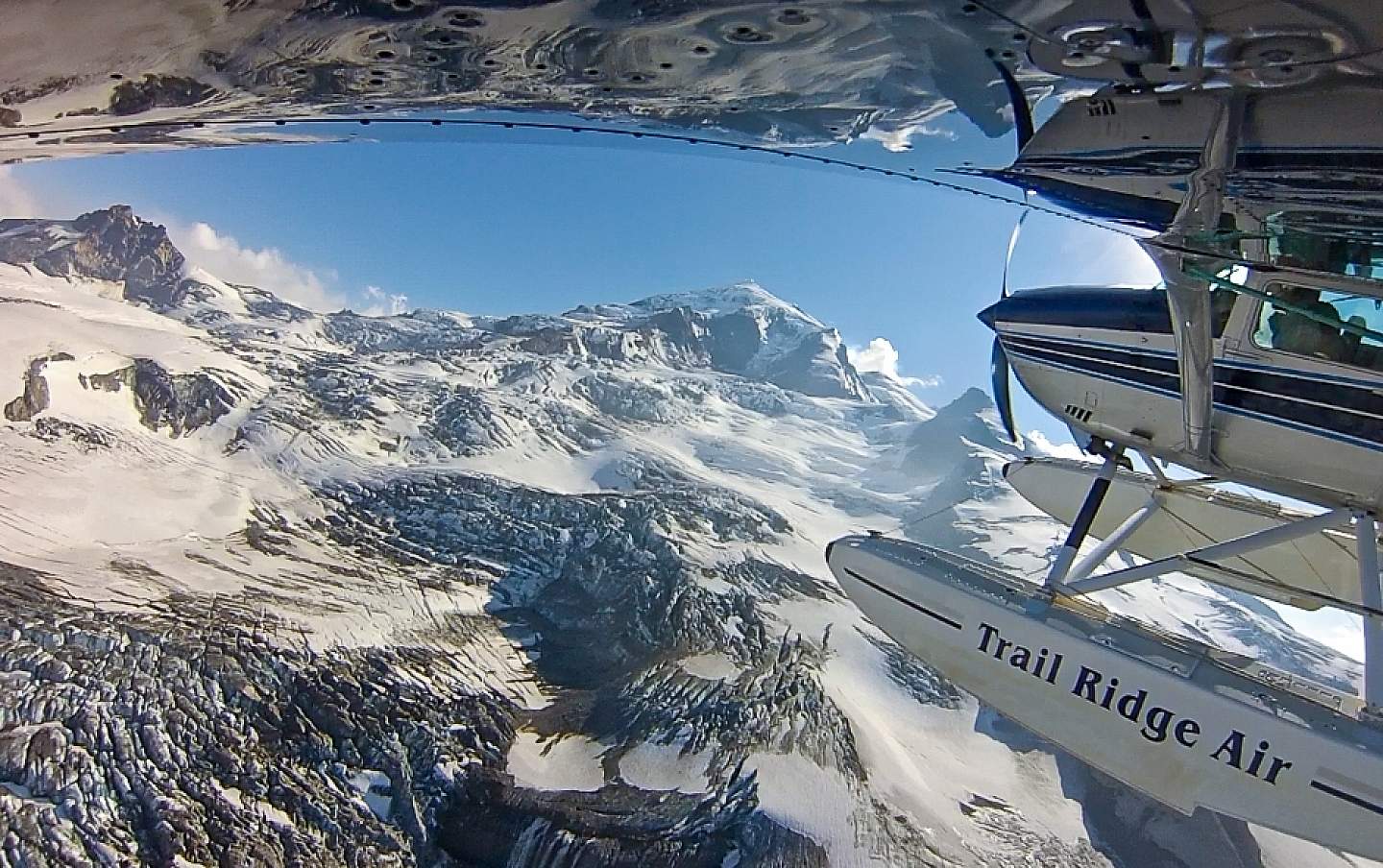 A view from under the wing of a bush plane as it flies above snow covered mountains.