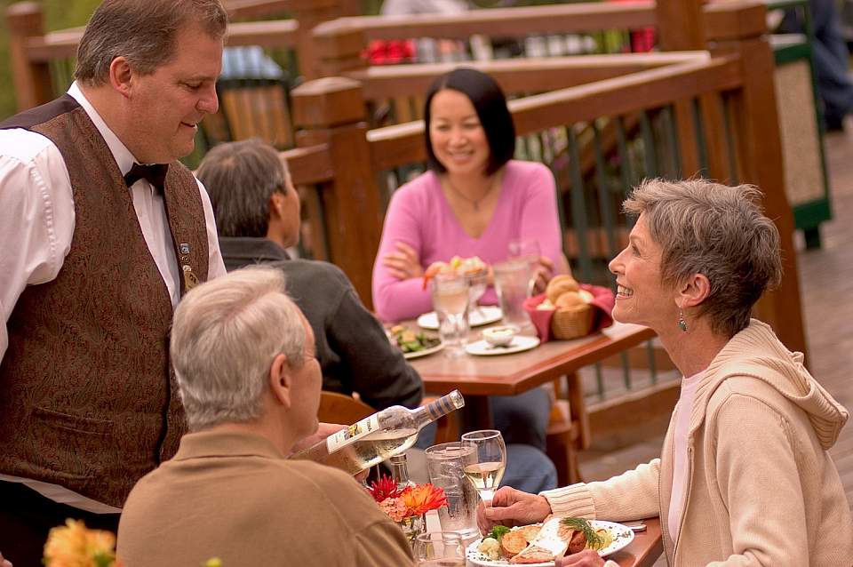 A server refills a glass of wine for a table of people on an outside deck.