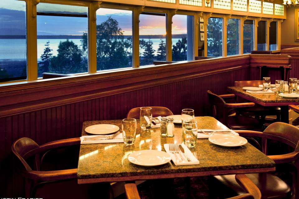 A set dining table in Simon & Seafort's dining room with views of the ocean outside of the windows.