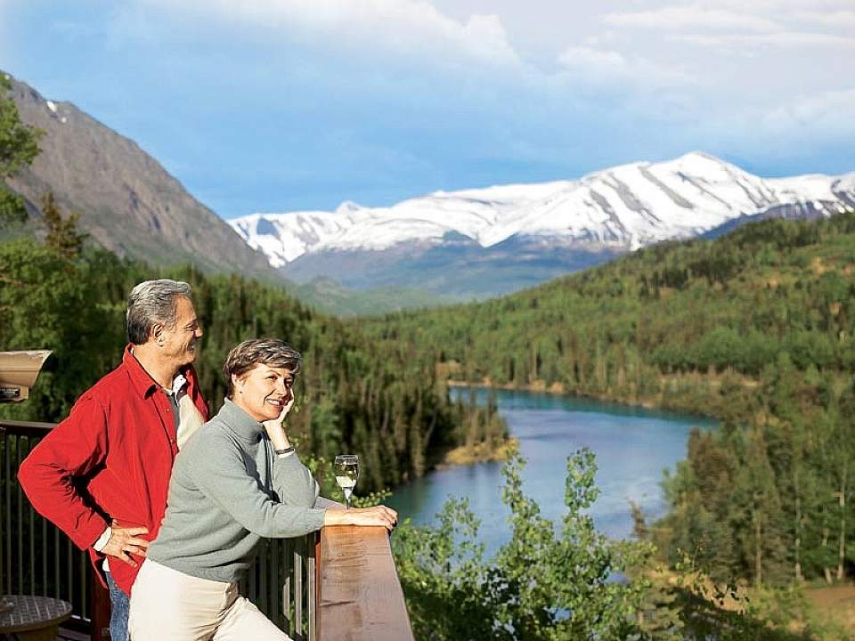 A couple stands at a viewing deck and looks out on the Kenai River Valley with mountains in the background.