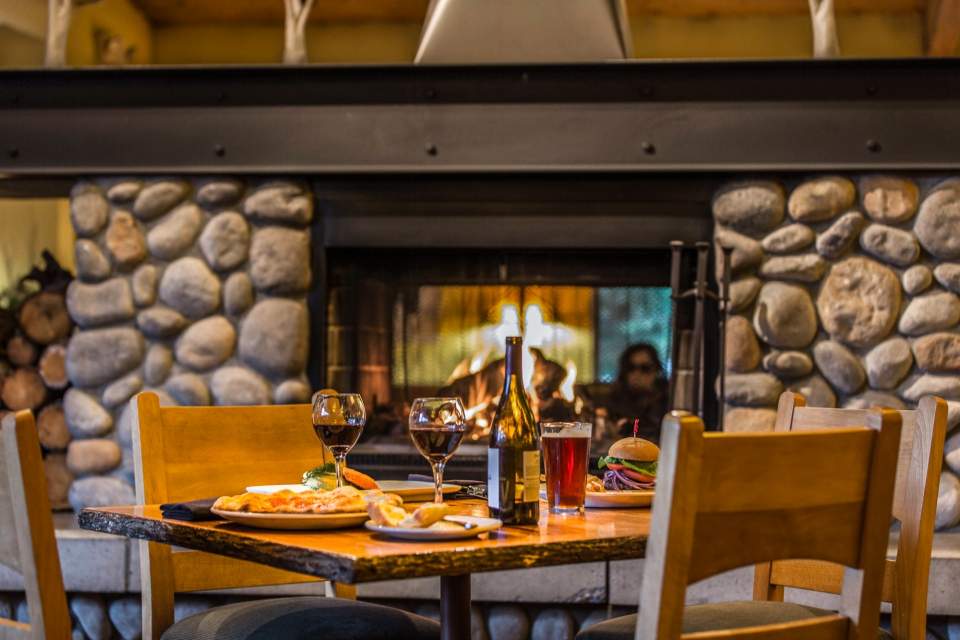 A restaurant table in front of a fire place set with food and wine.