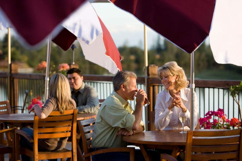 A smiling couple sits at a restaurant table outside overlooking the Chena River.