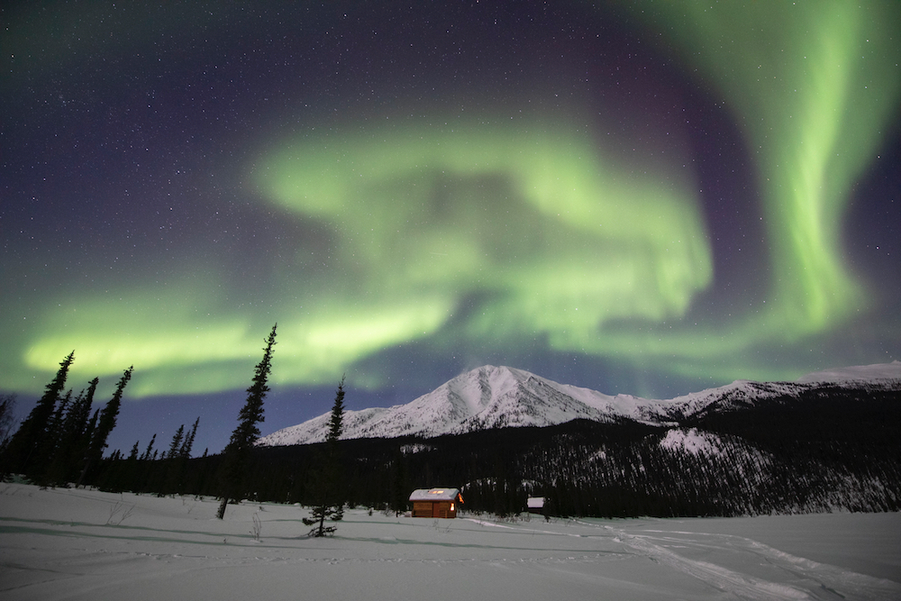 Iniakuk Lake Wilderness Lodge underneath a band of aurora on a winter night