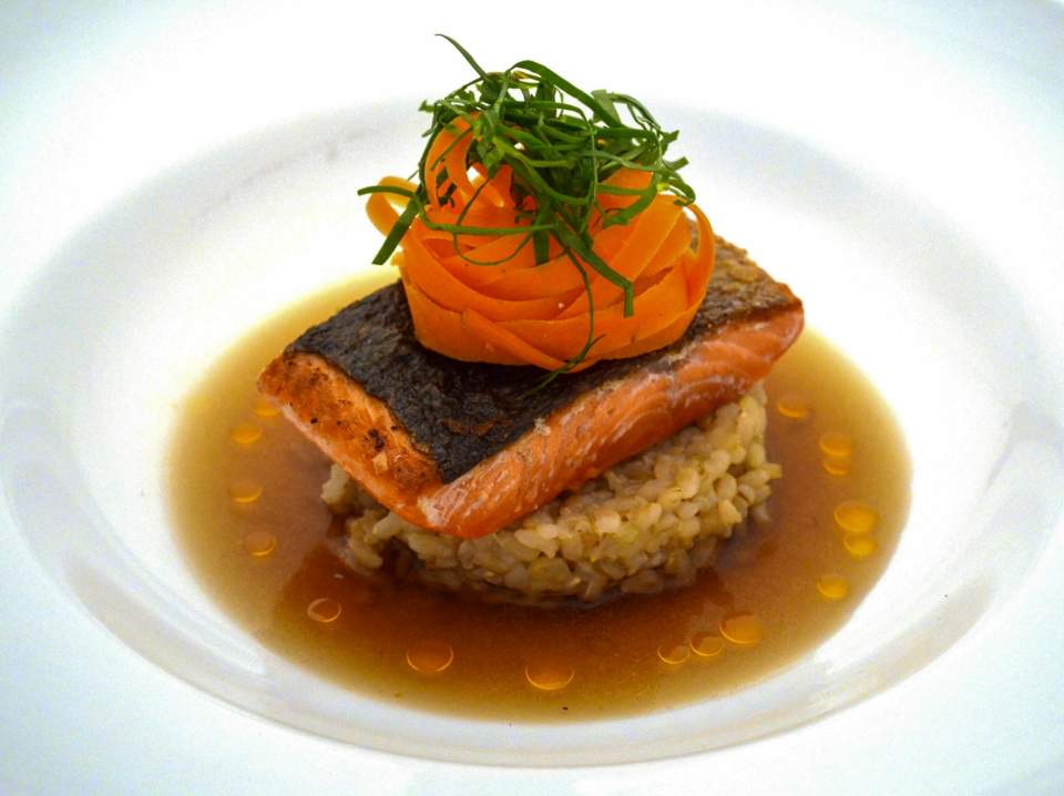 An beautiful dish of salmon resting on rice topped with swirled carrots and garnish.