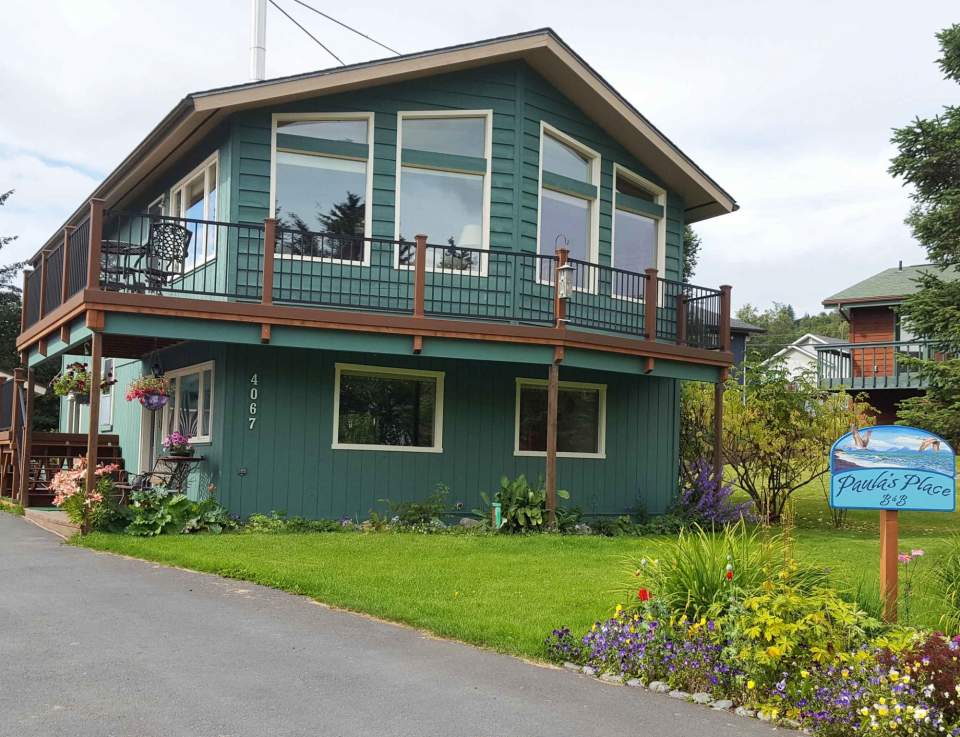 Outside of Paula's Place B&B, a green two story house with a yard full of flowers.