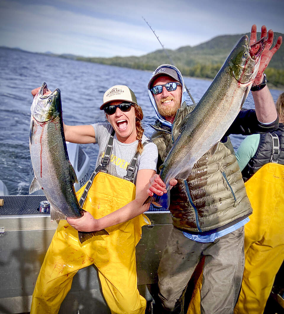 A couple holds up large salmon that they caught on a fishing charter from Salmon Falls Resort