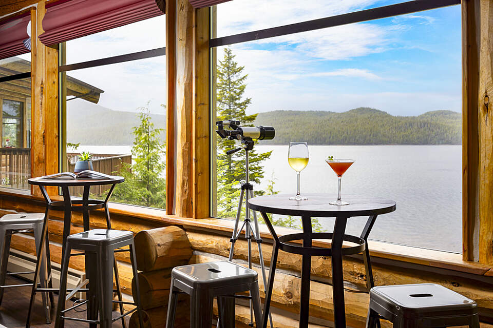 Two chairs by a high-top bar table with two wine glasses on top look out over the water from the restaurant at Salmon Falls Resort