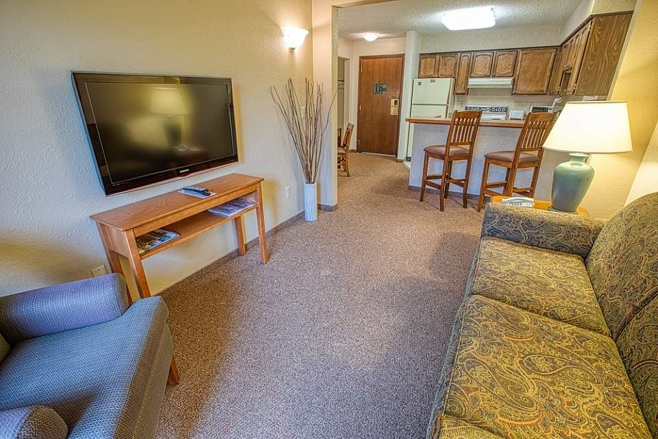 Inside a hotel suite look towards a full kitchen with two chairs at the bar.