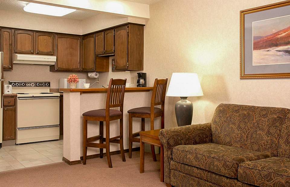 Inside a hotel suite look towards a full kitchen with two chairs at the bar.