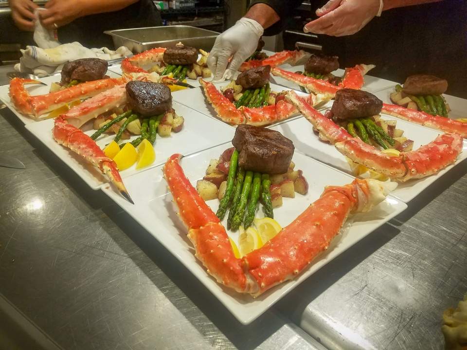 A cook arranges plates of surf and turf with vegetables.