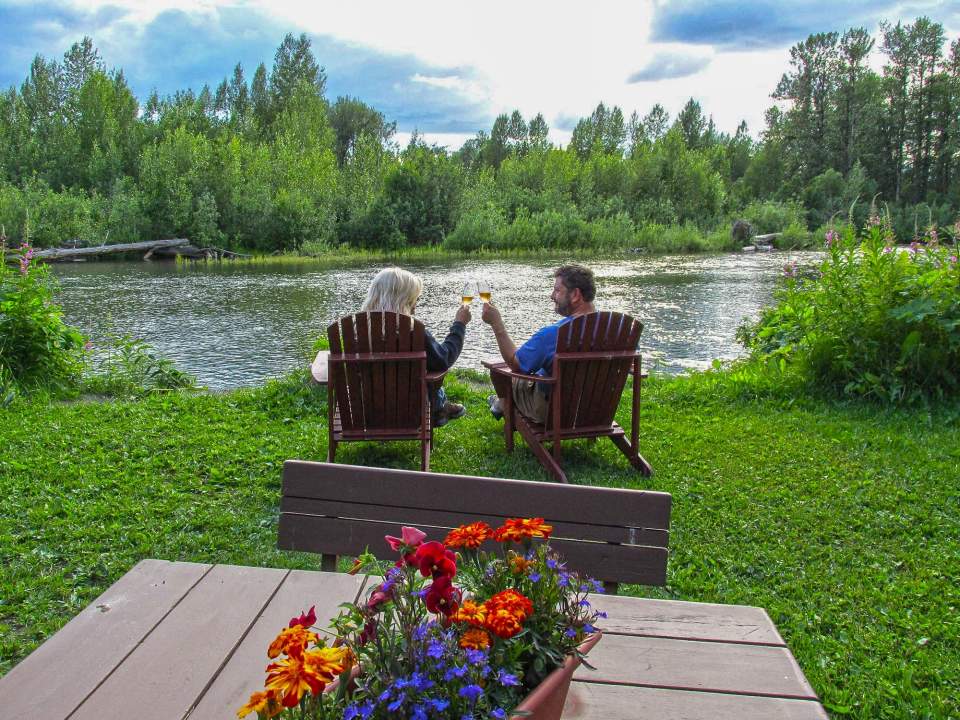 Two people in patio lounge chairs enjoy some wine together by the water.