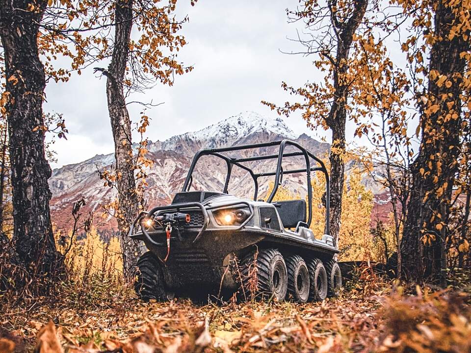 Image of the fully enclosed ARGO side by side in the woods with fall leaves and a snow capped mountain in the background